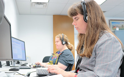 A person wearing headphones works at a computer in an office, focused on their screen